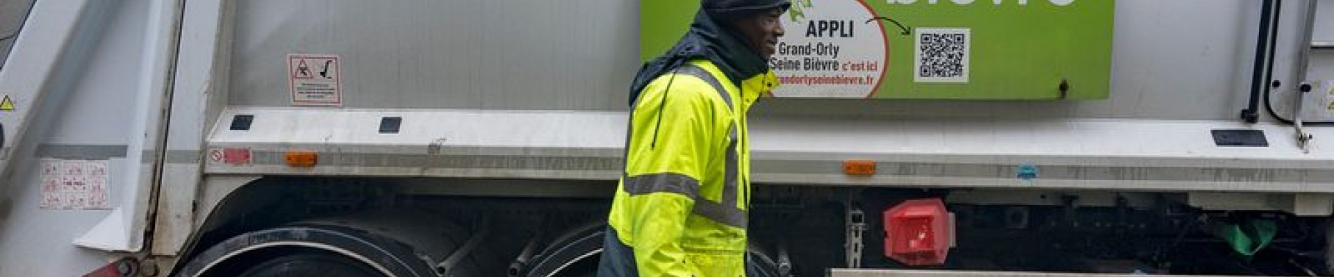 Un éboueur passe devant un camion poubelle en traînant un bac