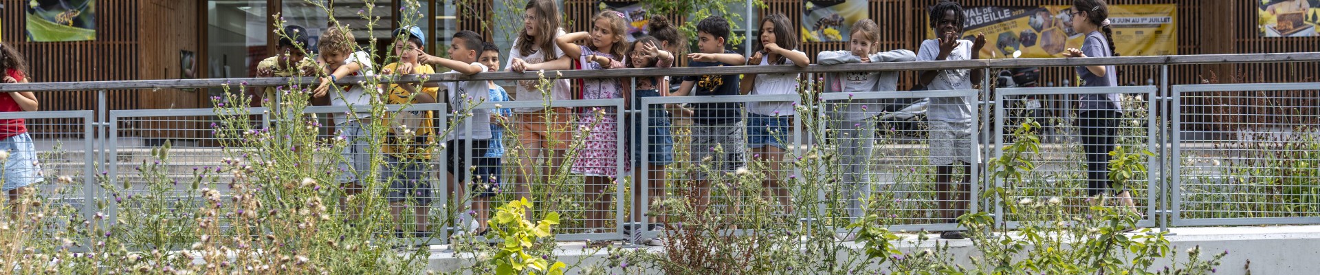 des enfants regardent la Bièvre, accoudés à une palissade, la Maison de l'Environnement en fond