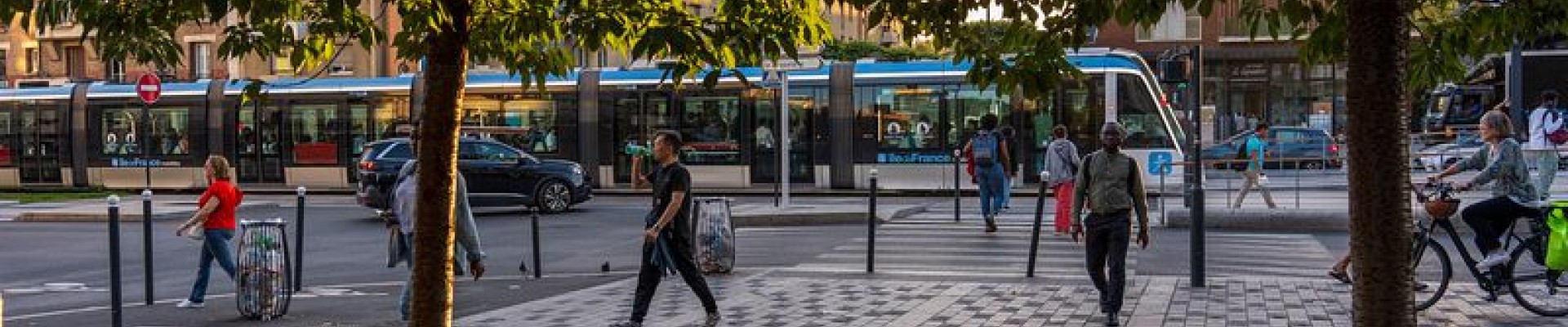 Des habitants marchent sur le trottoir, un tram en fond
