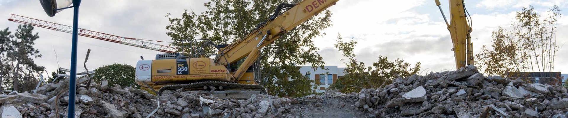 Palissage de chantier. Derrière un tractopelle manipule une montage de gravats issus d'un chantier de démolition.