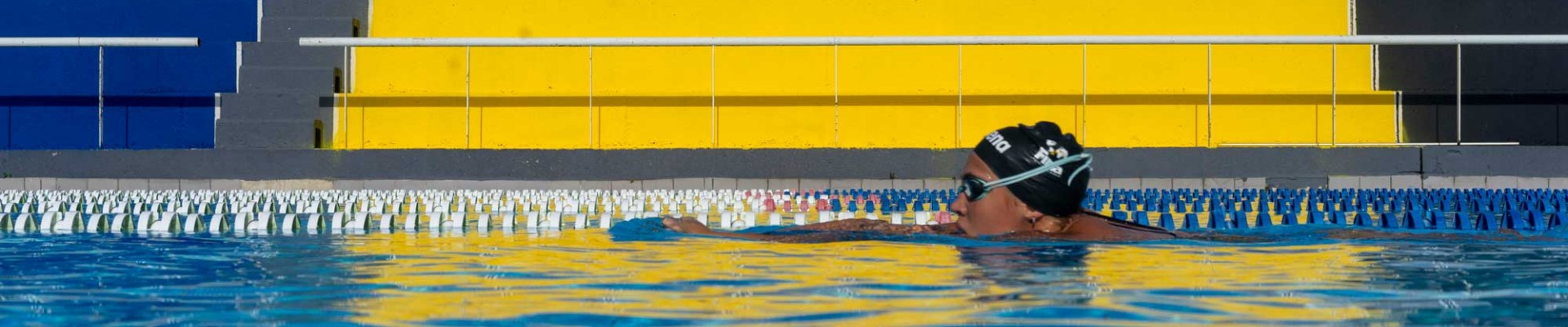 Vue au niveau de l'eau, la tête d'un nageur dépasse laissant apercevoir les gradins colorés du stade nautique Youri Gagarine à Villejuif