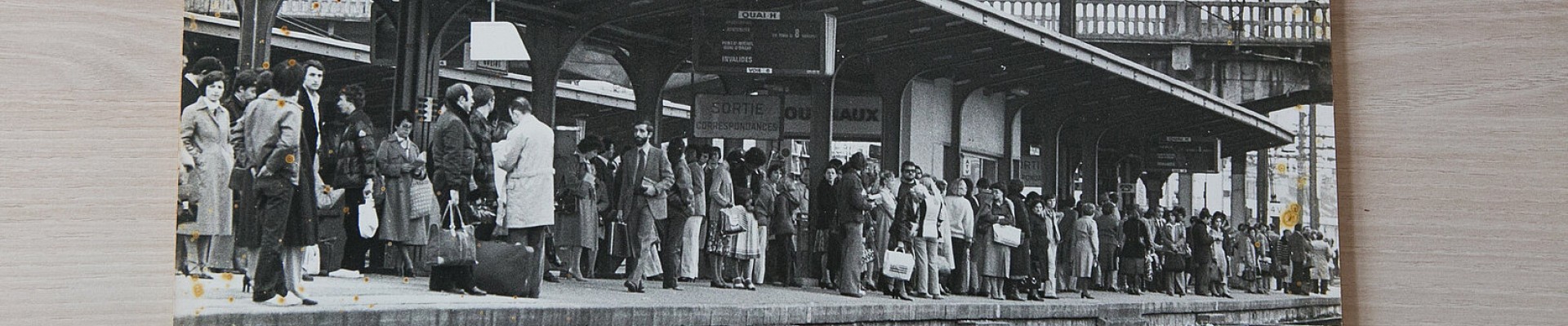 Photo en noir et blanc, tachée, représentant des voyageurs sur un quai de gare