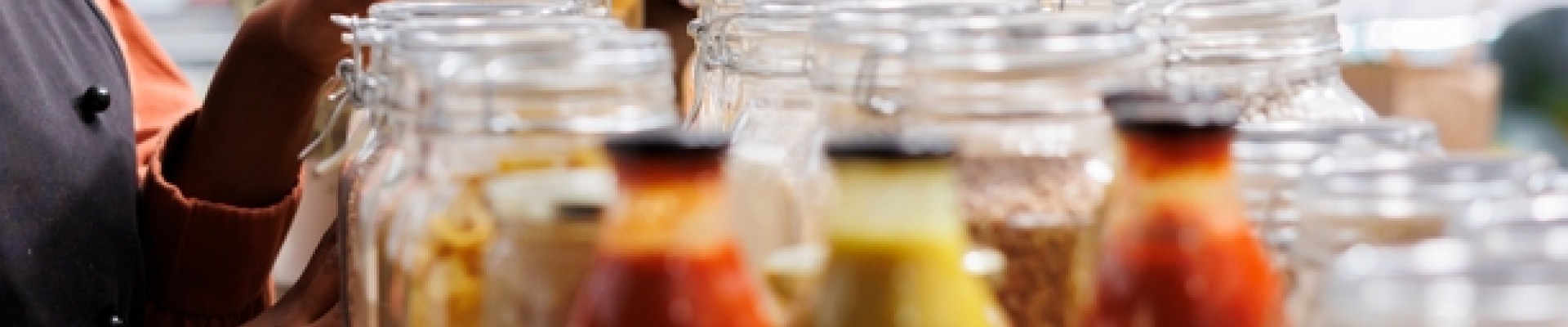 Une jeune femme souriante debout à côté d'une étagère en bois remplie de récipients en verre de nourriture en vrac