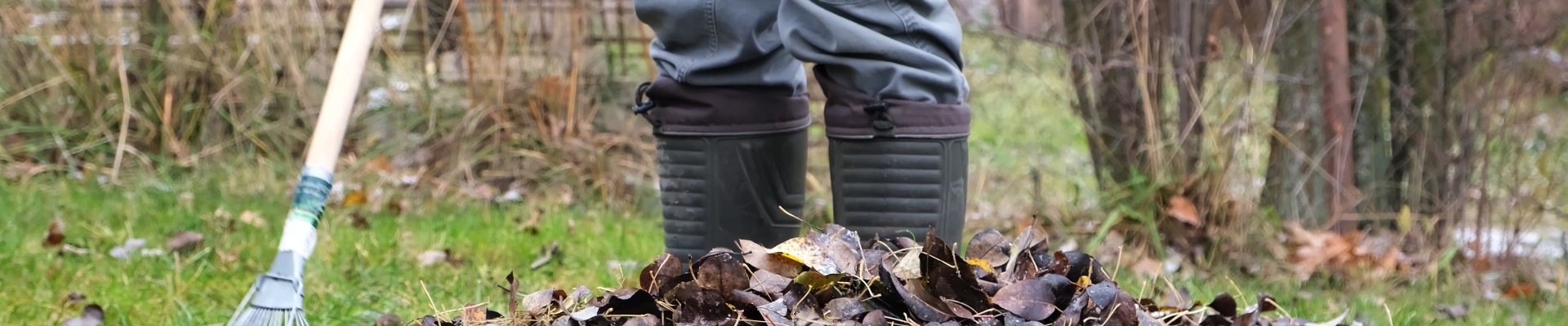 Un homme dont on ne voit que les bottes en caoutchouc ratelle des feuilles mortes