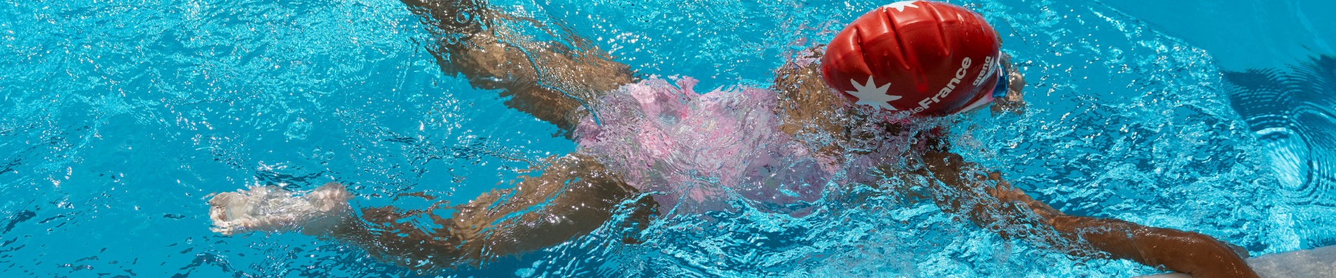 Enfant nageant sous l'eau en se tenant au bord dans le cadre des stages d'aisance aquatique pour favoriser l'apprentissage de la nage