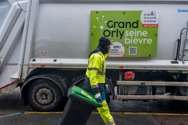Un éboueur passe devant un camion poubelle en traînant un bac