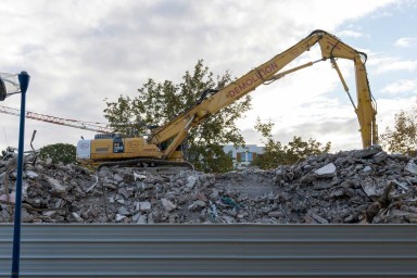 Palissage de chantier. Derrière un tractopelle manipule une montage de gravats issus d'un chantier de démolition.