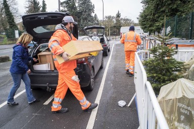 Agents de déchèterie mobile aidant un particulier à déposer des morceaux de meubles dans des enclos prévus pour ce type de déchet.