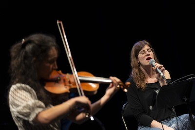 Une femme qui assise qui chante au micro accompagnée par une violoniste - Enlarge image 37 of 40, modal window