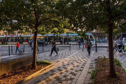 Des habitants marchent sur le trottoir, un tram en fond