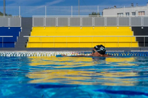 Vue au niveau de l'eau, la tête d'un nageur dépasse laissant apercevoir les gradins colorés du stade nautique Youri Gagarine à Villejuif