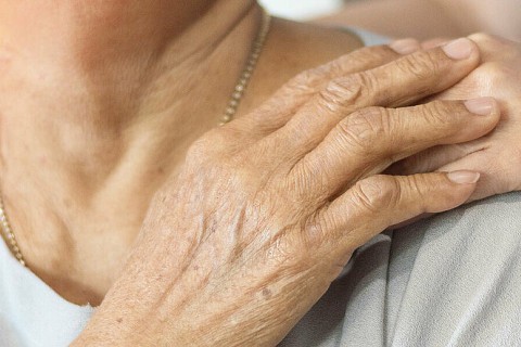 Main d'une personne âgée posée sur celle de son aidant 