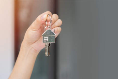 Une main tient une clé et un porte-clé en forme de maison