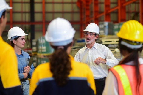 Des personnes portant un casque de chantier écoutent une personne avec des lunettes et un casque